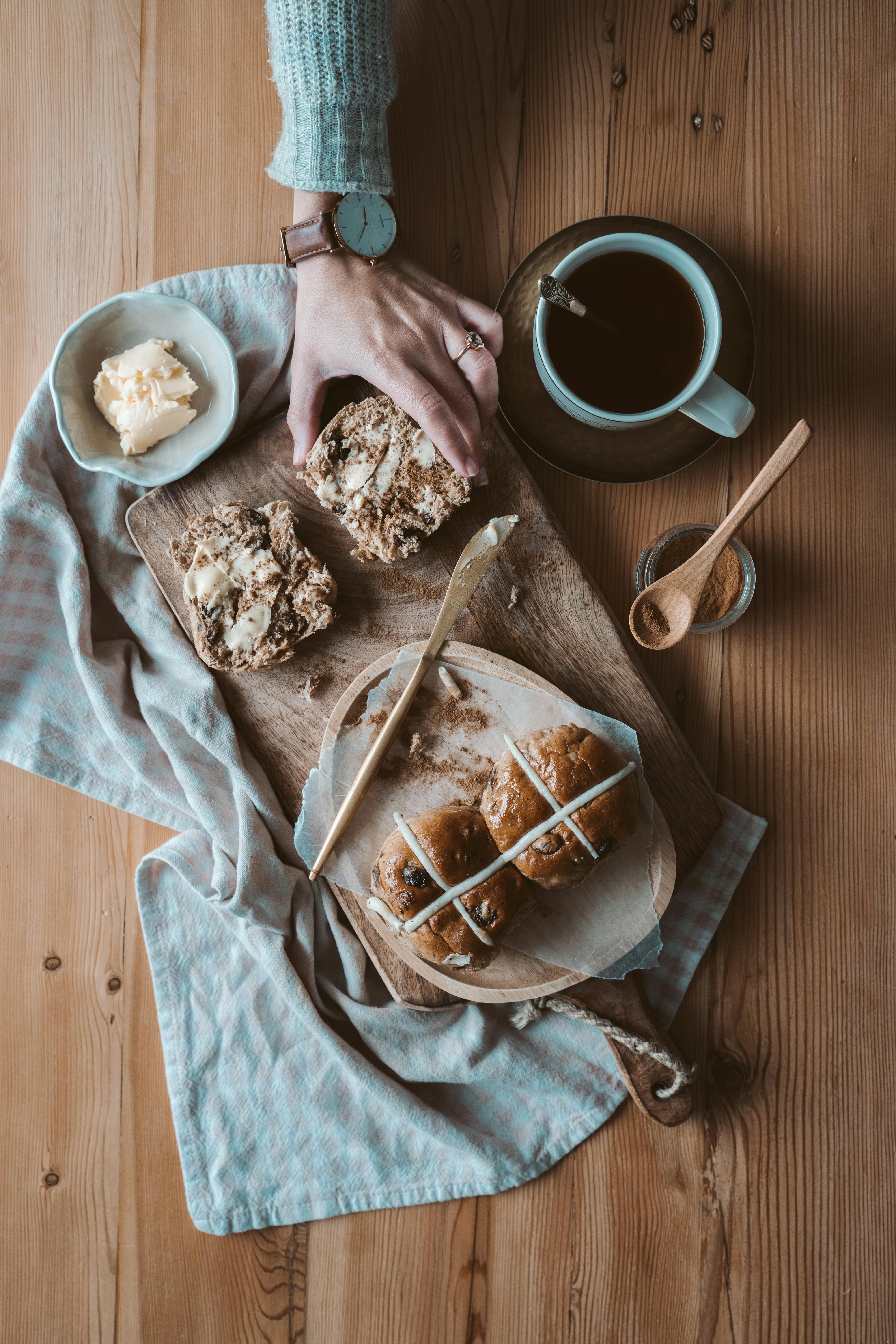 woman reaching for a buttered hot cross bun
